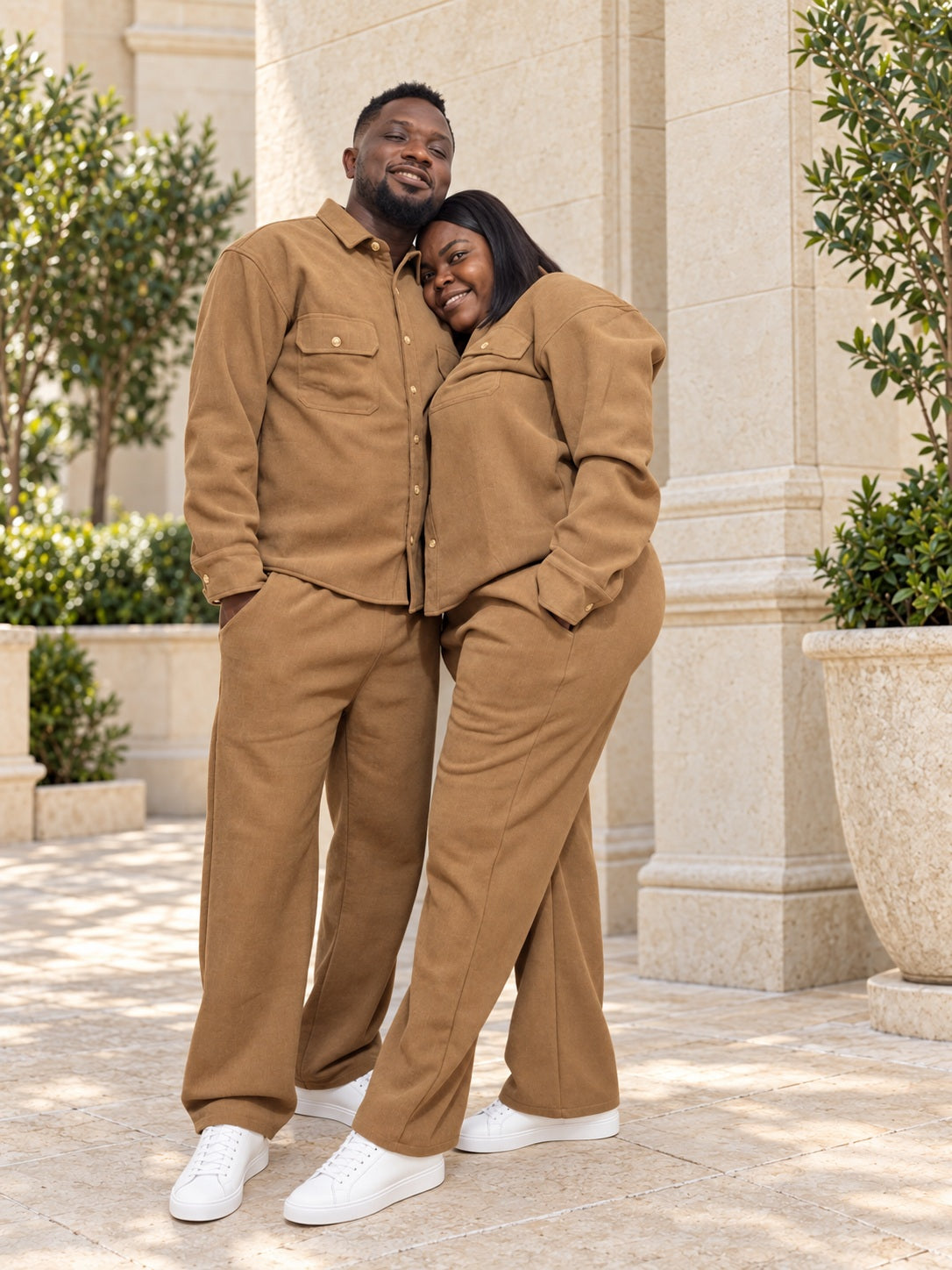 Couple portant les ensembles URIALEX brun caramel avec des baskets blanches assorties, dans une cour en pierre beige.