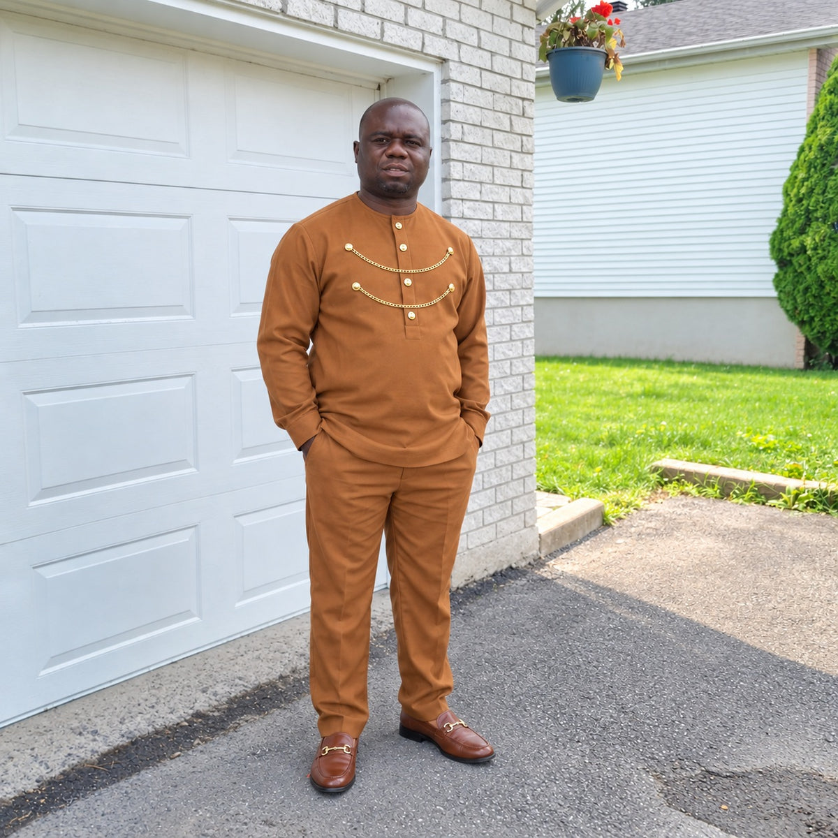 Homme portant l’ensemble tunique et pantalon URIALEX caramel à détails dorés et des mocassins bruns, devant un garage blanc.