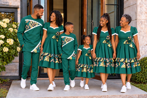 Famille de six personnes portant les tenues coordonnées URIALEX vert émeraude à motifs dorés, robes et ensembles tunique-pantalon avec baskets blanches.